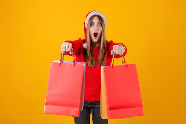 Mujer emocionada mostrando bolsas de compras navideñas rojas con sombrero de santa y suéter