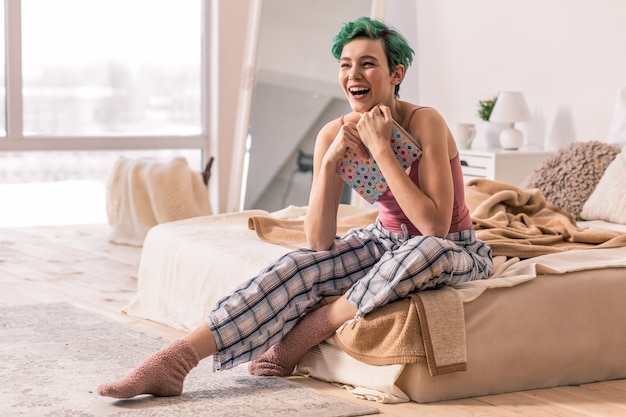 Mujer emocionada. Mujer de pelo verde que se siente emocionada antes del primer día de trabajo mientras está sentada en el dormitorio