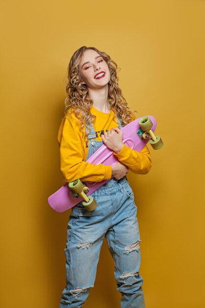 Mujer emocionada con patineta sobre un fondo amarillo brillante Emoción positiva