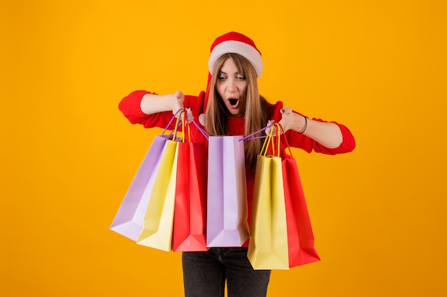 Mujer emocionada con regalos en bolsas de compras navideñas con gorro de santa y suéter