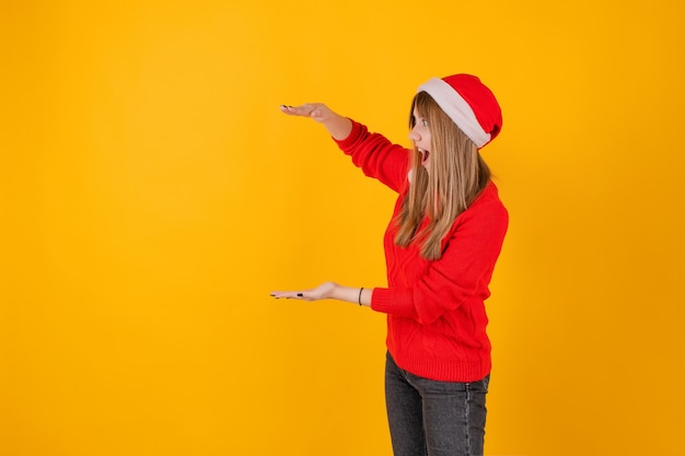 Mujer emocionada señalando copia espacio en mano vistiendo gorro de Papá Noel y suéter rojo