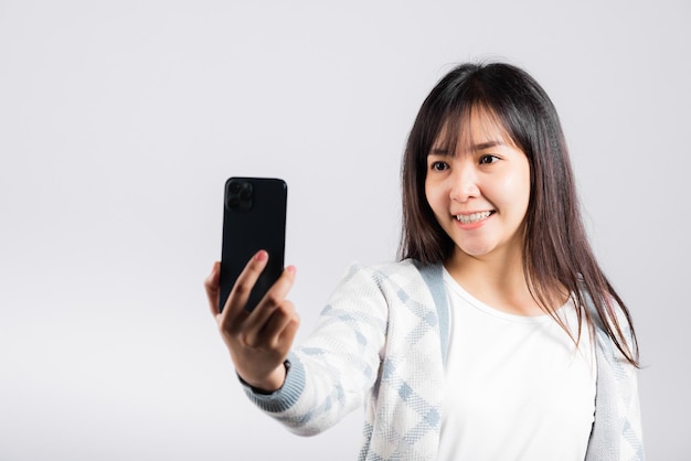 Mujer emocionada sosteniendo el teléfono inteligente para disparar una foto selfie en el estudio de la cámara frontal con un fondo blanco aislado, una joven feliz sonriendo tomando fotografías con un teléfono móvil en un teléfono móvil