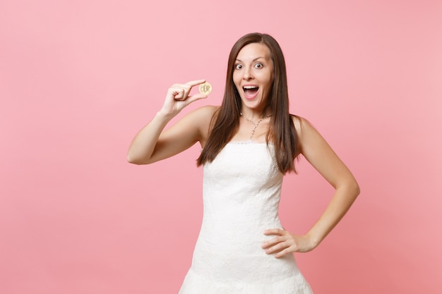 Mujer emocionada en vestido blanco con moneda de metal bitcoin de moneda futura de color dorado