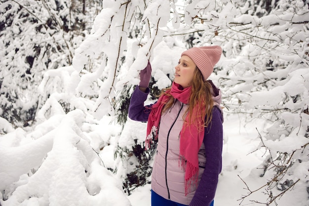 Mujer emocional de invierno con sombrero rosa divirtiéndose en el bosque con nieve