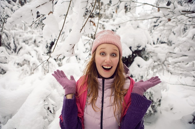 Mujer emocional de invierno con sombrero rosa divirtiéndose sorpresa en el bosque con nieve