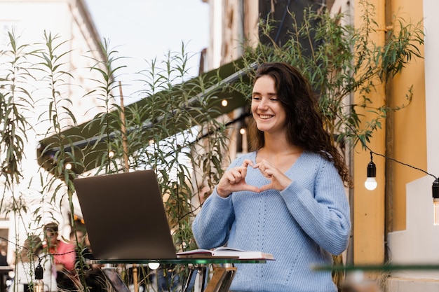 La mujer emocional sonríe y se comunica con amigos y se divierte a través de una conexión de video Una chica alegre con una laptop haciendo muecas y chatea por video con amigos y familiares en un café al aire libre