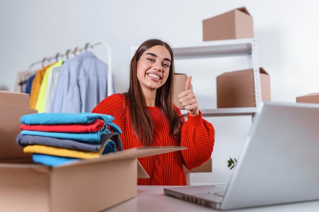 Foto mujer empacando un artículo que vende en línea. mujer trabajadora en la tienda online. llevaba ropa informal y comprobaba la dirección de la computadora portátil del cliente y la información del paquete. hermosa chica mostrando ok