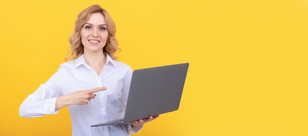 Mujer emprendedora feliz con camisa blanca señalando con el dedo a la computadora portátil en la presentación de fondo amarillo