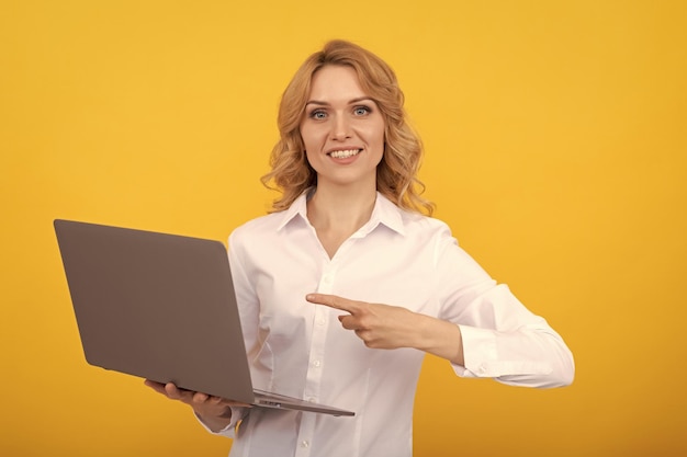 Mujer emprendedora feliz con camisa blanca señalando con el dedo a la computadora portátil en la presentación de fondo amarillo