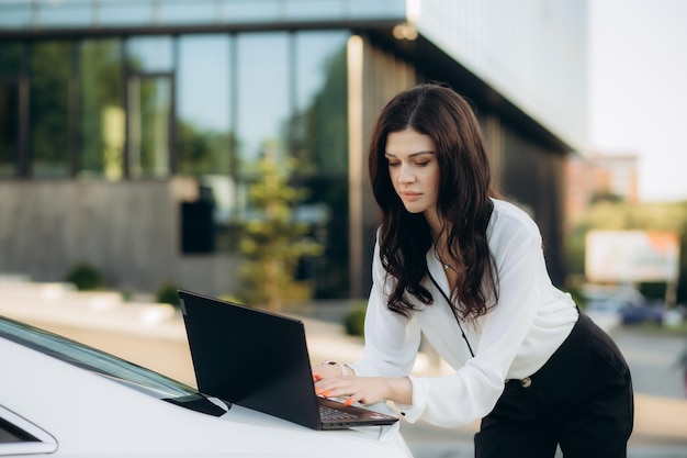 Mujer empresaria trabajando en una computadora portátil afuera en el fondo de un edificio moderno