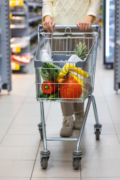 Mujer empuja un carrito en un supermercado y elige comida y comestibles una mujer europea en una tienda de comestibles