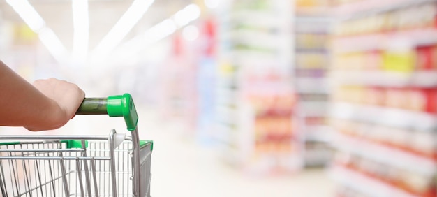 Mujer empujando carrito de compras con desenfoque de fondo de pasillo de supermercado