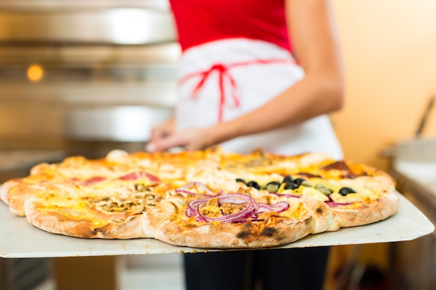 Mujer empujando la pizza terminada del horno