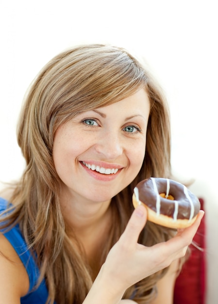 La mujer encantada está comiendo un donut en un sofá