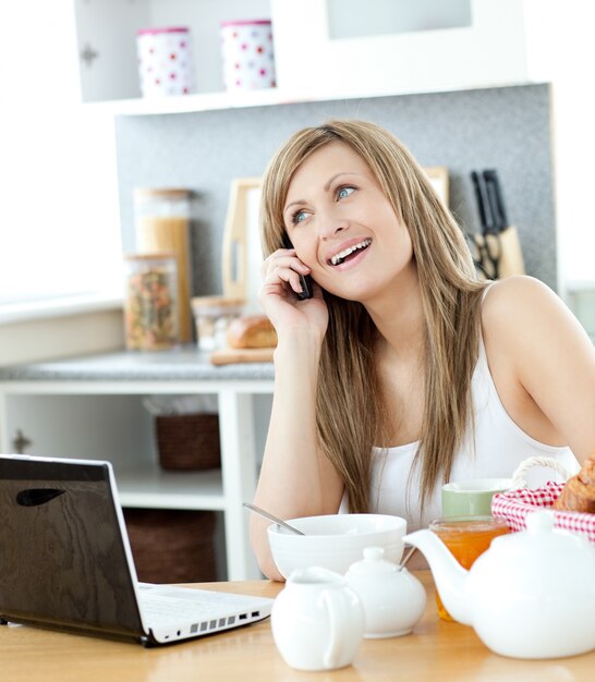 Mujer encantada usando un teléfono y una computadora portátil en la cocina