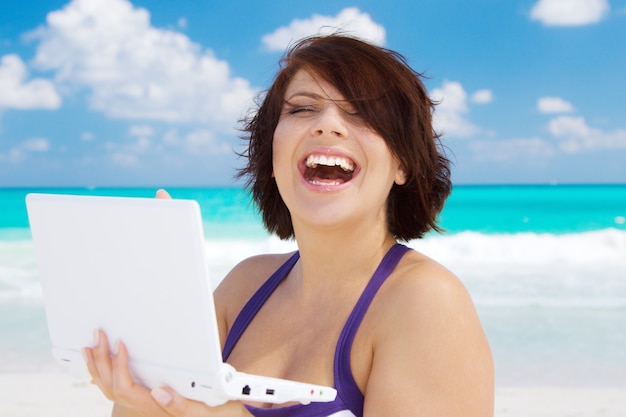 Mujer encantadora con ordenador portátil en la playa