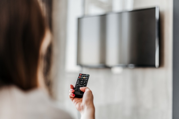 Mujer encendiendo la televisión con un control remoto en su casa en el apartamento