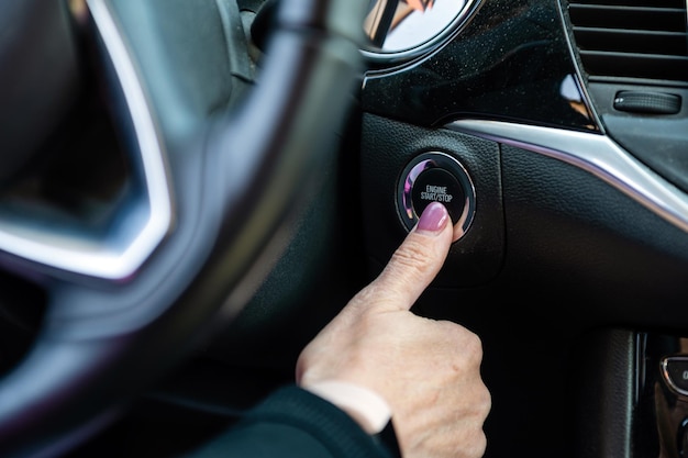 Mujer enciende el motor del coche con el botón de arranque-parada primer plano del interior del coche moderno