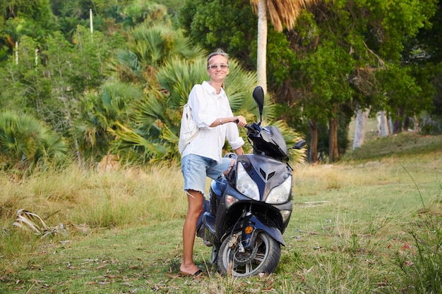 Mujer se encuentra cerca de un scooter en la naturaleza