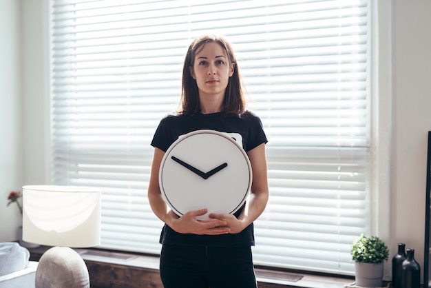 La mujer se encuentra en el escritorio y sostiene un reloj.