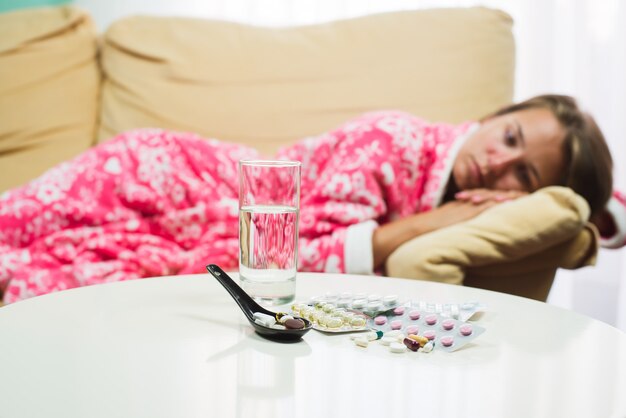 Foto mujer enferma acostada en la cama en bata mirando termómetro y pastillas