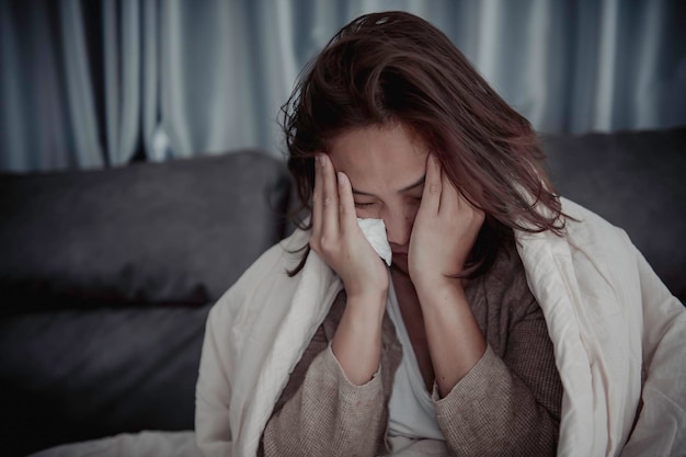 Una mujer enferma asiática se sienta en el sofá y se queda en casa. La mujer se sentía mal porque quería acostarse y descansar con fiebre alta.