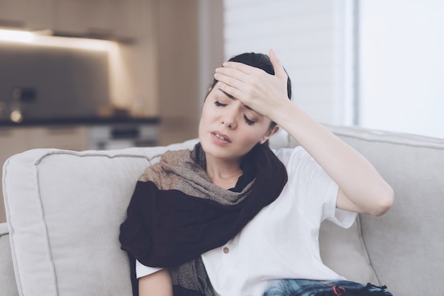 Mujer enferma está sentado en un sofá con un dolor de cabeza.