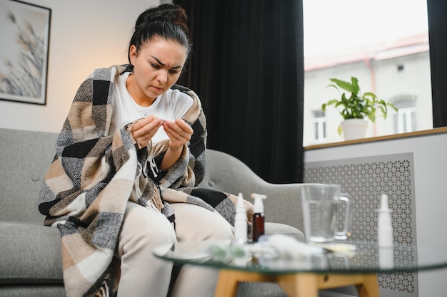 Mujer enferma con gripe Mujer atrapada en un estornudo frío en el tejido Medicinas para el virus del dolor de cabeza Mujer enferma con dolor de cabeza sentada en un sofá