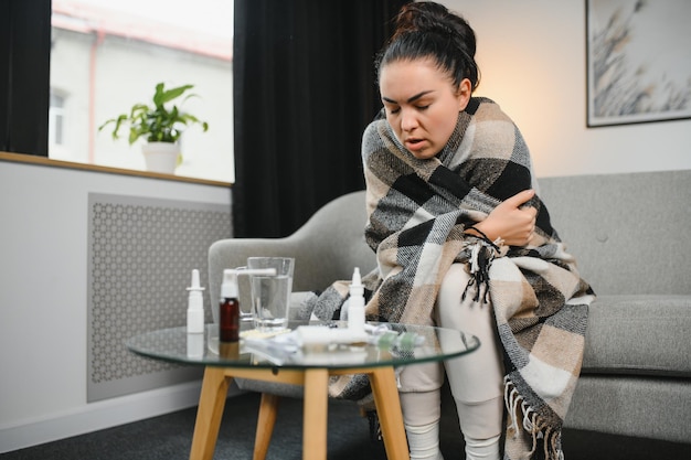 Mujer enferma con gripe Mujer atrapada en un estornudo frío en el tejido Medicinas para el virus del dolor de cabeza Mujer enferma con dolor de cabeza sentada en un sofá