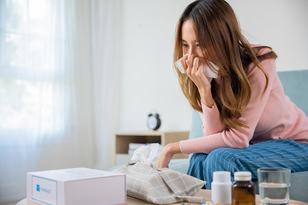 mujer enferma Hermoso problema de salud femenino que sopla la nariz usa el servicio de entrega de la caja del kit de farmacia del hospital, el concepto de farmacia de entrega, la joven asiática enferma de frío estornuda con papel de seda en el sofá