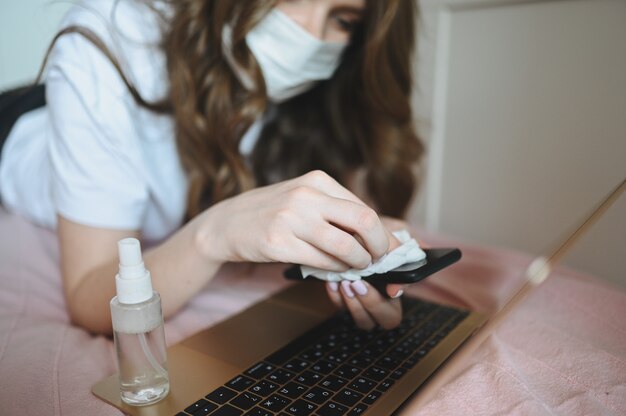 Mujer enferma con mascarilla en la cama durante el aislamiento de coronavirus limpieza de cuarentena en el hogar teléfono inteligente