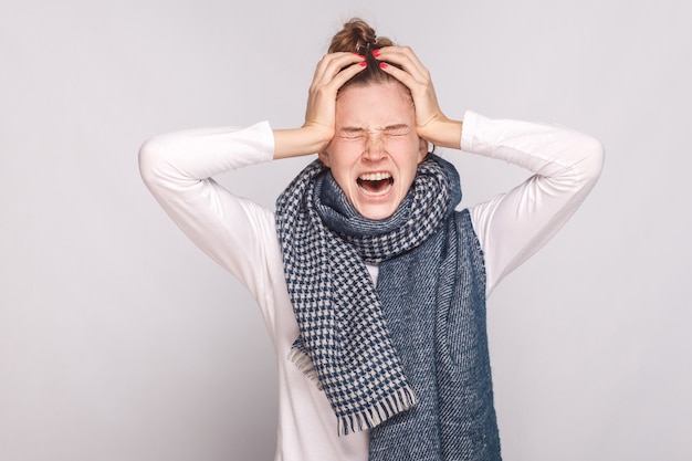 La mujer enferma tiene temperatura, se sostiene la cabeza y llora. Foto de estudio, aislado sobre fondo gris