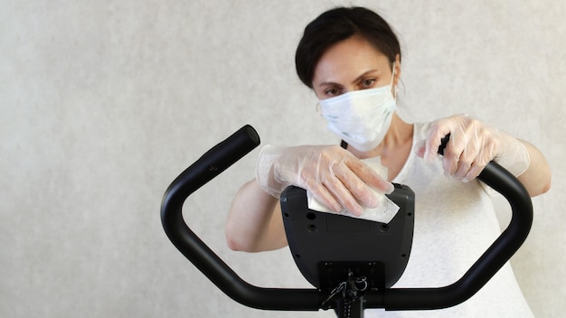 Una mujer enmascarada limpia el simulador con una toallita desinfectante para evitar la propagación del virus. Detener el coronavirus. COVID-19. lugar para el texto copia espacio