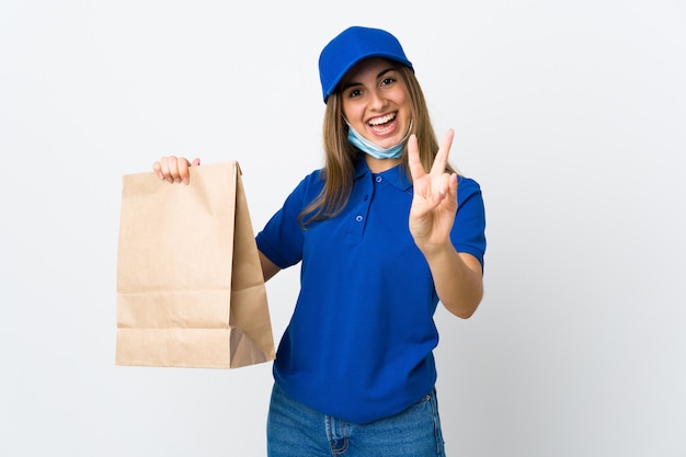 Mujer de entrega de alimentos y protección contra el coronavirus con una máscara sobre fondo blanco aislado sonriendo y mostrando el signo de la victoria