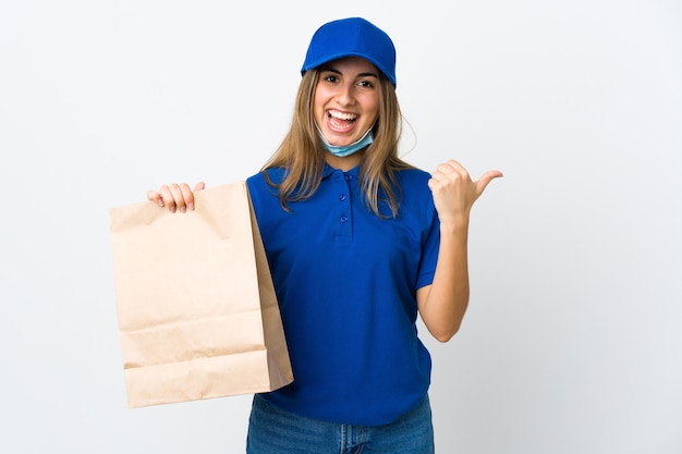 Mujer de entrega de alimentos y protección del coronavirus con una máscara sobre una pared blanca aislada que apunta hacia un lado para presentar un producto