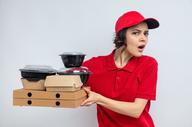 Mujer de entrega bonita joven despistada sosteniendo envases de comida y embalaje en cajas de pizza