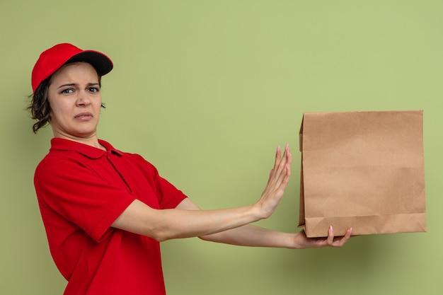 Mujer de entrega bonita joven disgustada sosteniendo una bolsa de comida de papel y mirando