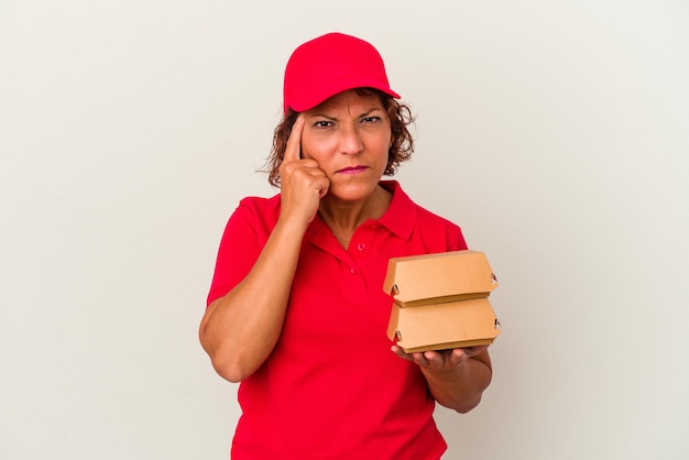 Mujer de entrega de mediana edad tomando burguers aislado sobre fondo blanco señalando la sien con el dedo, pensando, centrado en una tarea.