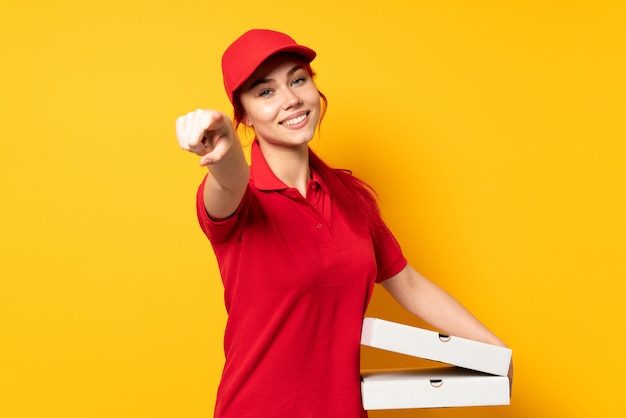 Mujer de entrega de pizza sosteniendo una pizza sobre pared aislada apuntando al frente con expresión feliz