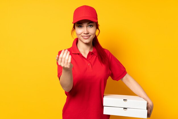 Mujer de entrega de pizza sosteniendo una pizza sobre pared aislada invitando a venir con la mano.