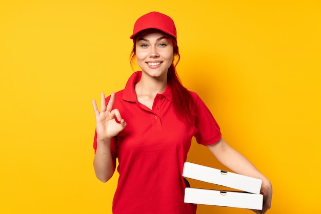 Mujer de entrega de pizza sosteniendo una pizza sobre una pared aislada que muestra un signo bien con las dos manos