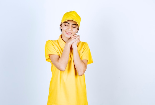 Mujer de entrega en uniforme amarillo de pie con los ojos cerrados contra la pared blanca.