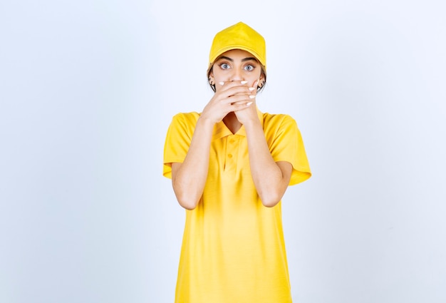 Mujer de entrega en uniforme amarillo de pie y tapándose la boca con las manos.