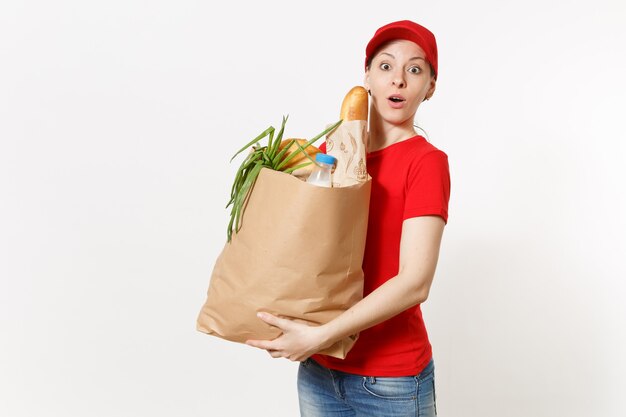 Mujer de entrega en uniforme rojo aislado sobre fondo blanco. Mensajero femenino en gorra, camiseta, jeans con paquete de papel con comida. Entrega de productos desde tienda o restaurante hasta su domicilio. Copie el espacio.