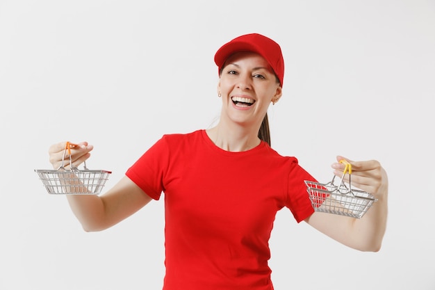 Mujer de entrega en uniforme rojo aislado sobre fondo blanco. Mensajero femenino o distribuidor en gorra, camiseta, jeans con canasta de metal para ir de compras en el supermercado. Copie el espacio para publicidad.