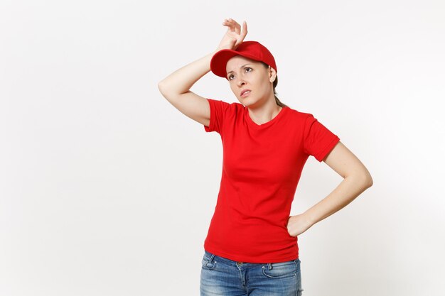 Mujer de entrega en uniforme rojo aislado sobre fondo blanco. Mujer sorprendida profesional con gorra, camiseta, jeans trabajando como mensajero o distribuidor, puso su mano en el gesto de la cabeza. Copie el anuncio del espacio.