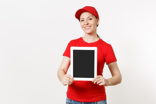 Mujer de entrega en uniforme rojo aislado sobre fondo blanco. Sonriente mujer con gorra, camiseta, jeans trabajando como mensajero o distribuidor, mostrando tablet pc con pantalla vacía en blanco a la cámara. Copia espacio