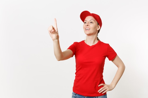 Mujer de entrega en uniforme rojo toque algo como hacer clic en el botón aislado sobre fondo blanco. Mujer con gorra, camiseta, jeans trabajando como mensajero o distribuidor, apuntando a la pantalla flotante. Copie el espacio.