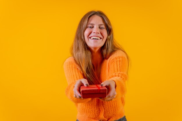 Una mujer entregando un regalo como sorpresa en un fondo amarillo