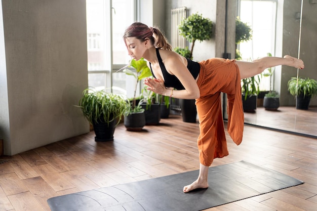 Una mujer entrena en un gimnasio en la pose de mat asana hace yoga en ropa deportiva